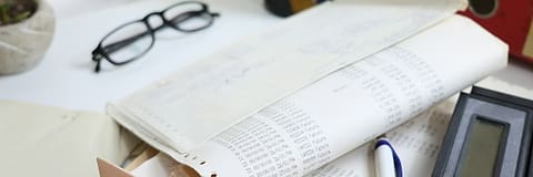 An open ledger, reading glasses and a pen on a working desk.