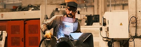 A welder at work on a steel part in a fabrication workshop.